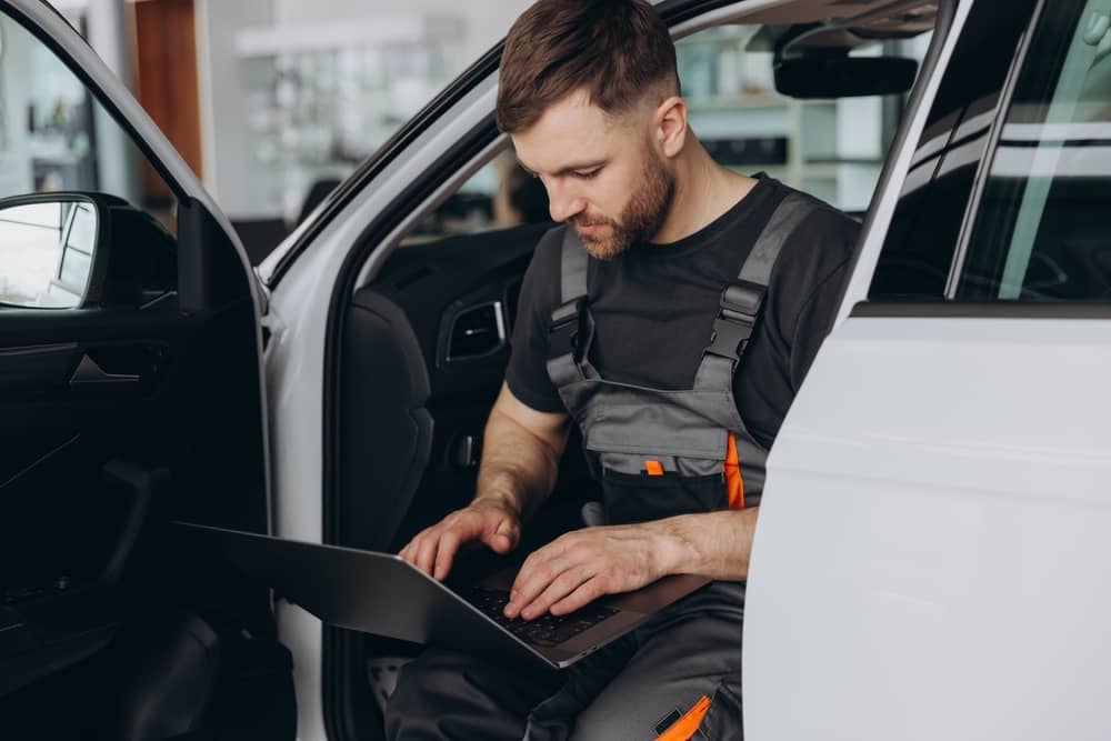 A man with an open car doing something about his laptop which is somehow related to dealer management software.