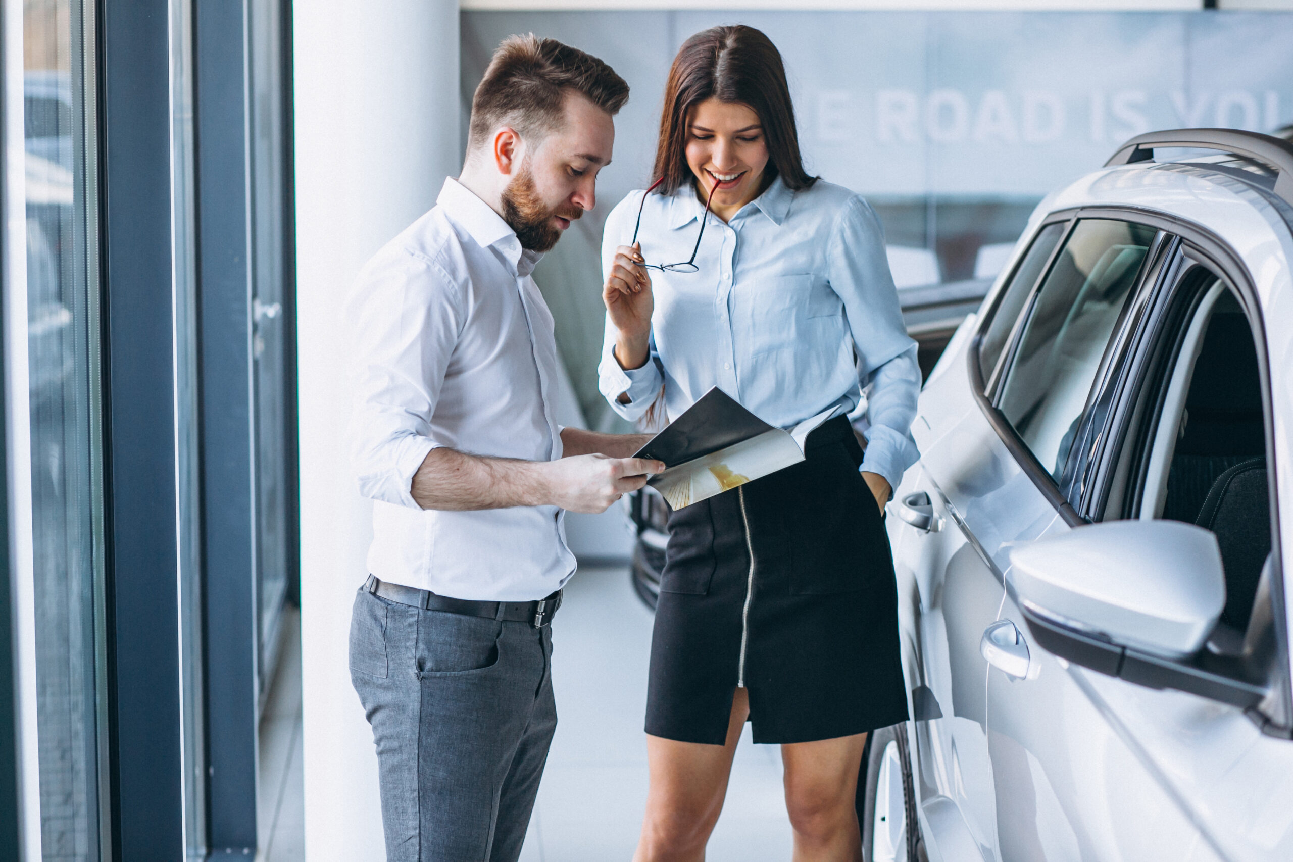 Image of a car dealership professional reviewing financial paperwork and discussing profits with a client, illustrating the process of determining new car dealer profit.