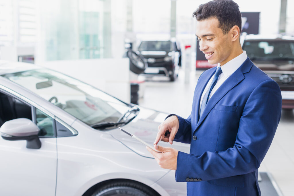 A man holding a tablet at a car dealership, representing strategies to maximize trade-in value for vehicles.