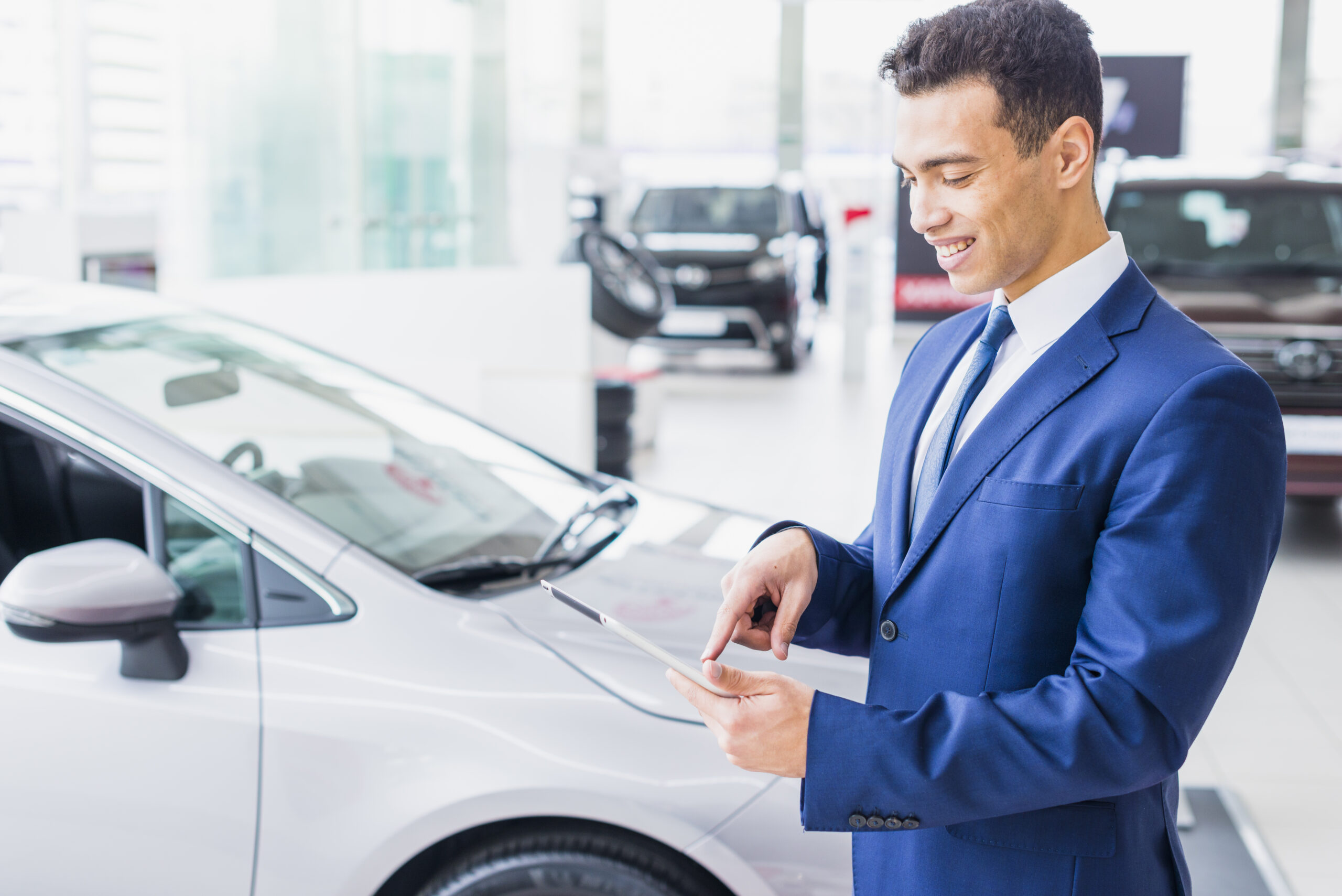 A man holding a tablet at a car dealership, representing strategies to maximize trade-in value for vehicles.